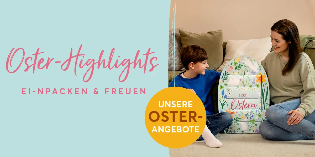 Mutter und Sohn sitzen in einem gemütlichen Wohnzimmer vor dem Sofa auf dem Boden. Zwischen ihnen steht das bunt dekorierte, riesiges brandnooz Osterei mit der Aufschrift "Frohe Ostern". Das Ei ist fast genauso groß wie der etwa 8 jährige Junge.