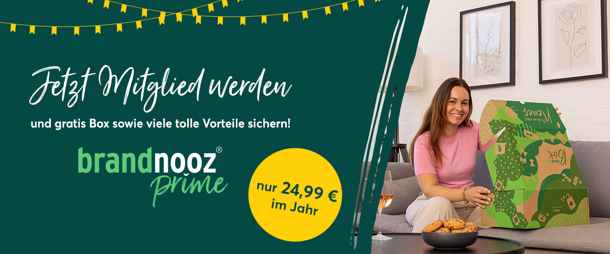 Auf dem Banner steht links: neu, brandnooz Prime, Jetzt Mitglied werden und Gratis Box, sowie viele Vorteile sichern. Rechts sitzt eine Frau auf einer Couch und freut sich, eine brandnooz Box zu öffnen.