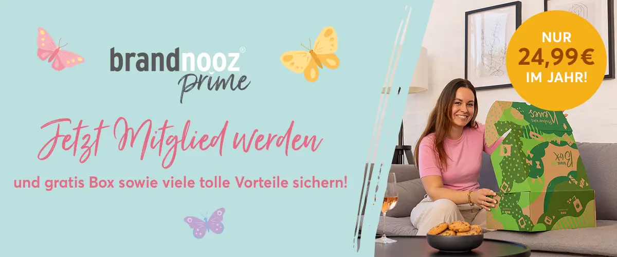 Auf dem Banner steht links: neu, brandnooz Prime, Jetzt Mitglied werden und Gratis Box, sowie viele Vorteile sichern. Rechts sitzt eine Frau auf einer Couch und freut sich, eine brandnooz Box zu öffnen.